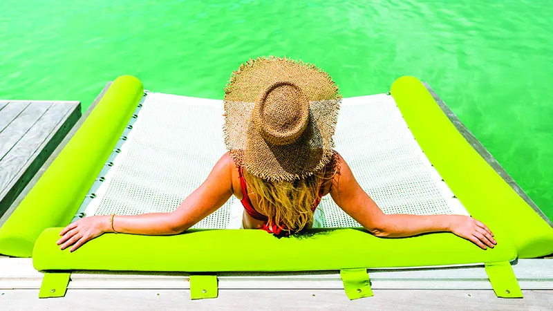A woman wearing a sun hat and bathing suit is relaxing in an overwater bungalow at Royal Caribbean’s private island, Perfect Day at CocoCay.